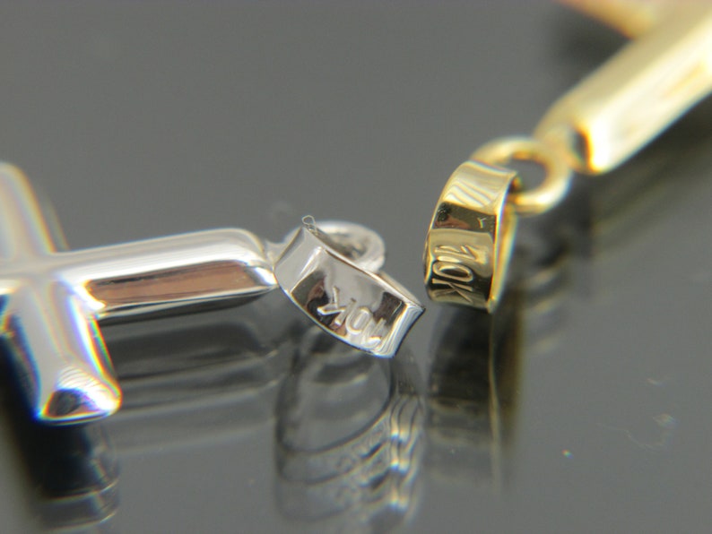 May include: A close-up of a silver cross pendant with a 10K hallmark. The pendant is attached to a gold chain.