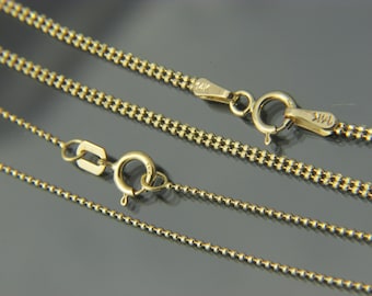 May include: Two gold chains with a ball chain design. The chains are laying on a gray surface. The chain on top has a clasp with the marking "14K".