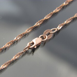 May include: Rose gold-colored necklace with a twisted rope chain design. The clasp and connecting ring are visible, with the word "ITALY" stamped on the ring. The chain is displayed against a dark, reflective surface.