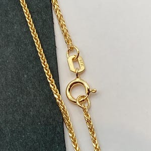 May include: A gold chain necklace with a lobster clasp. The chain is a delicate, braided design. The clasp is marked with "14K".