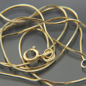 May include: A gold snake chain necklace with a lobster clasp. The necklace is made of thin, flexible links. The clasp is marked "10K". The chain is displayed on a reflective surface. The necklace is a classic jewellery item.