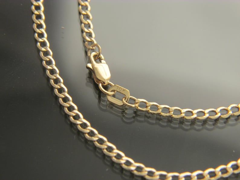 K&ouml;nnte beinhalten: Eine goldene Kettenkette mit einem Karabinerverschluss. Die Kette ist im Curb-Stil und hat einen 10K-Stempel am Verschluss.