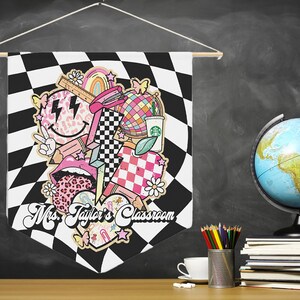 Pode incluir: Uma bandeira de pennant em xadrez preto e branco com um design rosa, branco e preto que apresenta um rosto sorridente, l&aacute;bios, um cora&ccedil;&atilde;o xadrez, um arco-&iacute;ris, um globo terrestre e uma x&iacute;cara de caf&eacute;. A bandeira diz "Mrs. Taylor's Classroom".