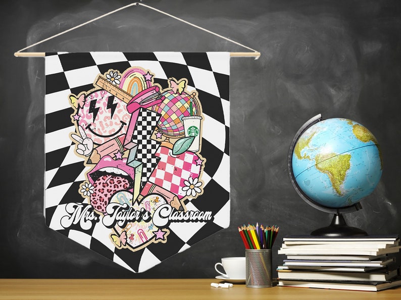 Pode incluir: Uma bandeira de pennant em xadrez preto e branco com um design rosa, branco e preto que apresenta um rosto sorridente, l&aacute;bios, um cora&ccedil;&atilde;o xadrez, um arco-&iacute;ris, um globo terrestre e uma x&iacute;cara de caf&eacute;. A bandeira diz "Mrs. Taylor's Classroom".
