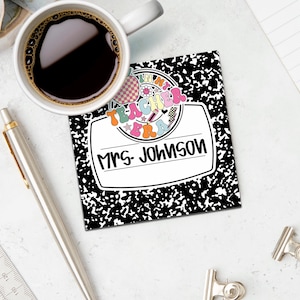 May include: A black and white composition notebook with the text "I'm in my teacher era" and "Mrs. Johnson" in a colorful, retro design. A cup of coffee, a pen, and a ruler are also visible.