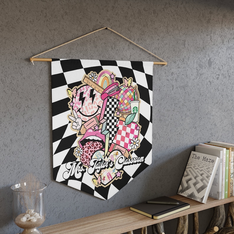 Pode incluir: Uma faixa xadrez preta e branca com um design rosa, branco e preto que apresenta um rosto sorridente, um arco-&iacute;ris, um grampeador, uma bola de discoteca, uma x&iacute;cara de caf&eacute;, um cora&ccedil;&atilde;o e um raio. A faixa diz "Mrs. Taylor's Classroom".