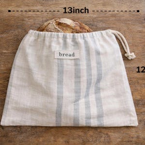 May include: A linen bread bag, 13 inches wide and 12 inches tall, with blue vertical stripes and a drawstring closure. The word "bread" is printed on a small label. A loaf of bread is visible inside the bag.