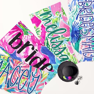 May include: Four colorful beach towels with the words "Bride", "Maid of Honor", "Bridesmaid", and "Macy" written in a whimsical font. The towels have a floral pattern with pink, blue, green, and white colors.