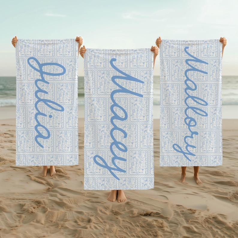 May include: Three white beach towels with blue patterned borders and blue cursive names "Julia", "Macey", and "Mallory" written on them.