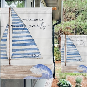 May include: A white garden flag with a blue and white striped sailboat, waves, and the text "welcome to sunny sails 1932".