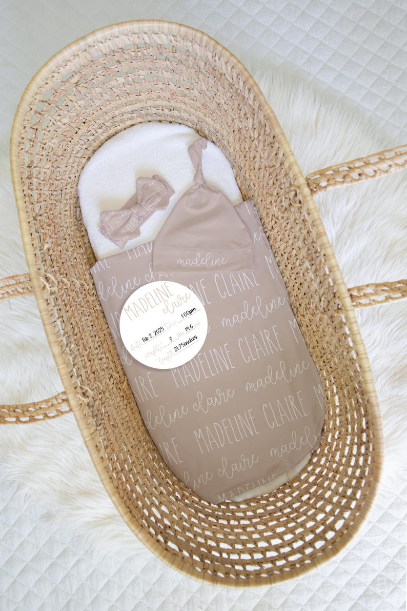 May include: A newborn baby set in a woven basket, including a blanket, hat, and bow. The blanket is taupe with the name "Madeline Claire" in a repeating pattern. A white circle displays the baby's birth details: date, time, weight, and length.