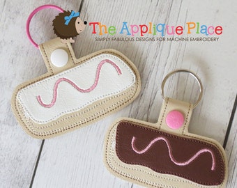Può includere: Due portachiavi dal design rettangolare, uno con parte superiore bianca e zig-zag rosa, l'altro con parte superiore marrone e zig-zag rosa. Entrambi hanno un bordo beige e un bottone a pressione rosa. Il testo The Applique Place è visibile.