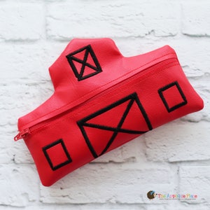 May include: A red pencil case shaped like a barn, featuring black embroidered details. The design includes a zipper closure and black geometric shapes resembling windows and a door. The pencil case is made of a smooth, possibly faux leather material.