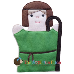May include: A felt hand puppet depicting a shepherd with brown hair and a green tunic. The puppet has a smiling face, a brown staff, and a brown rope belt. The text "The Applique Place" is at the bottom.