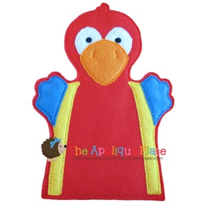May include: A red felt parrot puppet with a large orange beak, white eyes, and blue and yellow accents. The puppet has a simple design and is likely handmade. The text "the Applique Place" is visible.