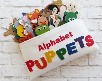 May include: A white zippered pouch with the words "Alphabet PUPPETS" in rainbow letters. The pouch is filled with felt finger puppets of various animals, including a deer, a frog, a fox, a penguin, a unicorn, and a sheep.