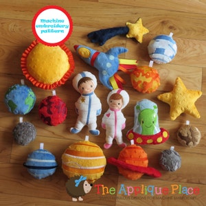 Op de afbeelding: Een verzameling kleurrijk, pluche speelgoed met ruimtethema, waaronder planeten, sterren, een raket en astronauten. Het speelgoed is gemaakt van vilt en stof, met geborduurde details. De tekst "Machine embroidery pattern" is zichtbaar.