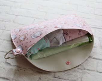 May include: A light pink, open diaper clutch with a guinea pig pattern. The clutch is filled with baby clothes and wipes. It has a heart-shaped ring and a snap closure. The interior is white.
