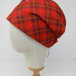 Puede incluir: Un sombrero con estampado de cuadros rojos y marrones. El sombrero está hecho de tela y tiene un cordón. El sombrero se exhibe en una cabeza de maniquí.