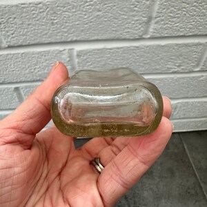 May include: A clear glass bottle with a rounded bottom and a slightly flared top. The bottle is empty and has a textured surface.