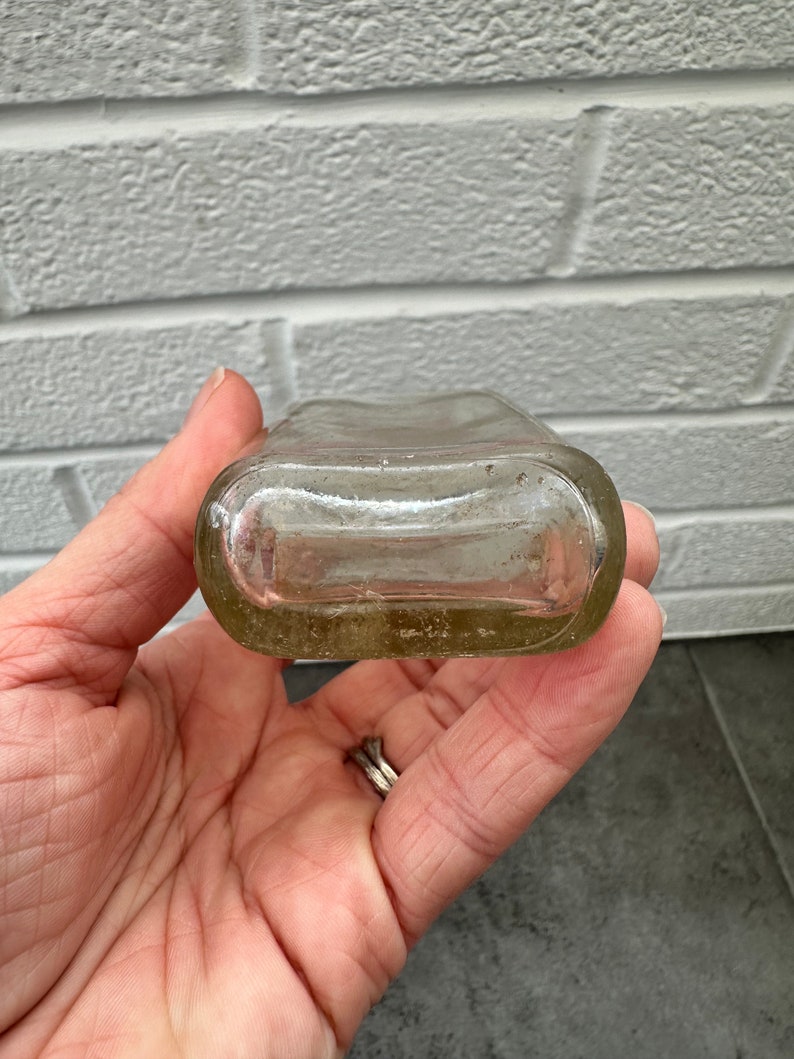 May include: A clear glass bottle with a rounded bottom and a slightly flared top. The bottle is empty and has a textured surface.