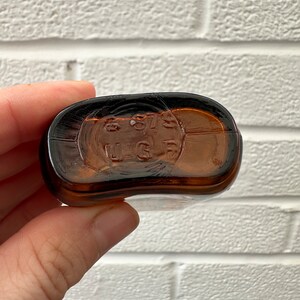 May include: Close-up of the bottom of a brown glass bottle with the text "8 97 U.S.G." embossed on the bottom.