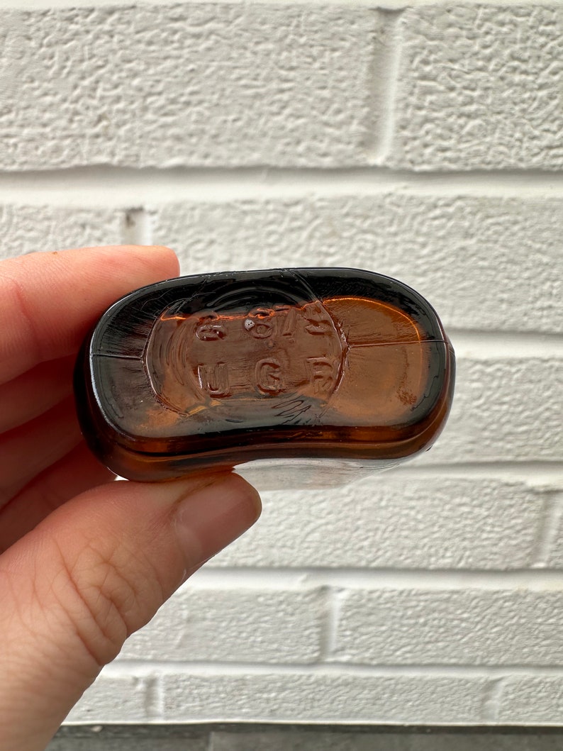 May include: Close-up of the bottom of a brown glass bottle with the text "8 97 U.S.G." embossed on the bottom.