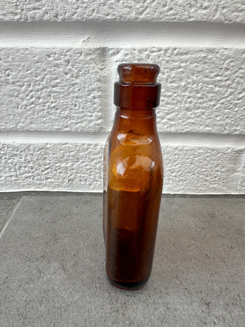May include: A brown glass bottle with a rounded bottom and a short neck. The bottle has a glass stopper and is empty.