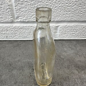 May include: A clear glass bottle with a rounded bottom and a slightly flared neck. The bottle is empty and appears to be vintage.