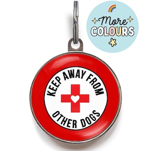 May include: A round, red dog tag with the text "KEEP AWAY FROM OTHER DOGS" in black. A red cross with a white heart is in the center. A smaller, light blue circle with the text "+More COLOURS" and a rainbow is in the upper right.