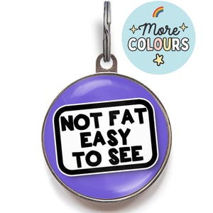 May include: Purple round dog tag with a silver ring. The tag has a white rectangle with black text that reads "NOT FAT EASY TO SEE".