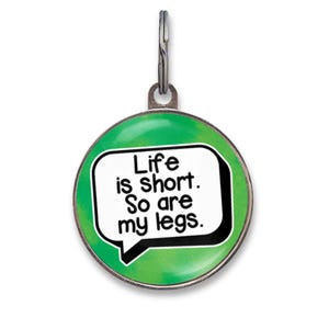 May include: A round, green pet ID tag featuring a white speech bubble with the black text, "Life is short. So are my legs." The tag has a metallic border and a silver-toned metal ring attached to the top loop for securing to a collar.