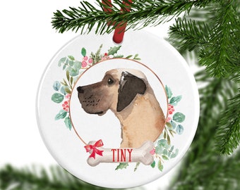 May include: A round white ceramic ornament featuring a watercolor illustration of a tan Great Dane in profile. The dog is framed by a copper circle and green holly leaves with red berries. A bone-shaped graphic with the red text TINY is below.