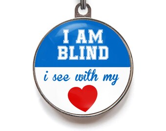 May include: A round, silver dog tag with a blue and white background. The tag says "I AM BLIND i see with my" with a red heart in the middle.