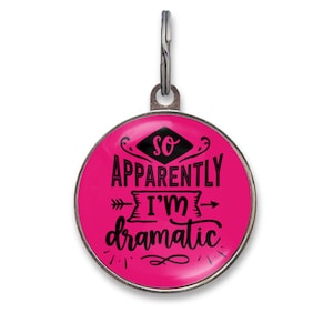 May include: A round metal pet ID tag with a bright pink background and black text that reads, So Apparently I'm Dramatic. The tag features a silver-toned metal border and a small metal ring at the top for attachment to a collar or keychain.