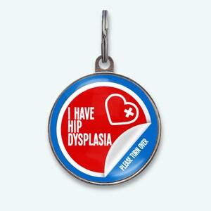 Op de afbeelding: Een ronde, zilverkleurige dierenpenning met een rood en blauw ontwerp. De penning toont de tekst "I HAVE HIP DYSPLASIA" en een wit hart met een kruis. De rechter benedenhoek heeft een afgepeld effect met de tekst "PLEASE TURN OVER".