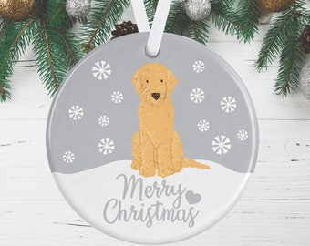 Op de afbeelding: Een rond keramieken ornament met een illustratie van een lichtbruine doodle-hond in het midden op een grijze achtergrond met witte sneeuwvlokken. Het onderste gedeelte is wit met de grijze tekst Merry Christmas en een klein hartje. Een wit lint is bevestigd.