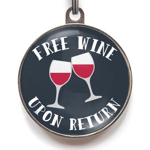 May include: A round, silver dog tag with a dark blue background. The tag features two wine glasses clinking, with the text "FREE WINE UPON RETURN" in white.