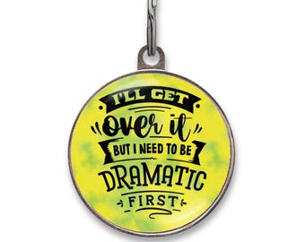 May include: A round metal pet ID tag with a yellow and green tie-dye background. The text reads I'LL GET OVER IT BUT I NEED TO BE DRAMATIC FIRST in black lettering. The tag features a silver metal border and a small silver split ring at the top.