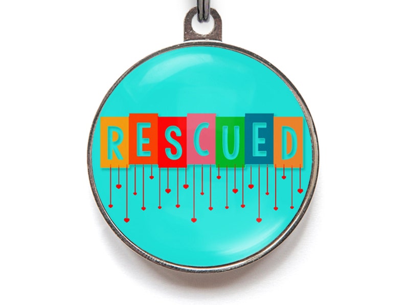 May include: A round, turquoise blue pet tag with a silver border. The word "RESCUED" is spelled out in colorful blocks with red hearts hanging from each letter.