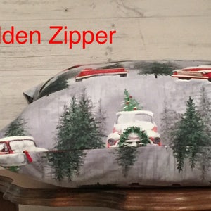May include: A gray pillow with a Christmas-themed print featuring red trucks with Christmas trees on top, surrounded by green trees. The pillow has a hidden zipper.
