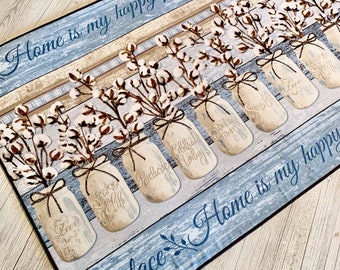 Puede incluir: Una alfombra de bienvenida azul y marrón con un diseño de veta de madera rústica. Presenta una fila de tarros de cristal llenos de ramitas de algodón y el texto "Home is my happy place" repetido dos veces.