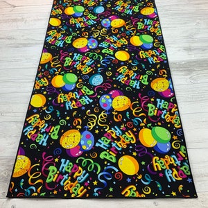 May include: Black table runner with a colorful pattern of balloons and confetti. The balloons have the text "Happy Birthday" on them.