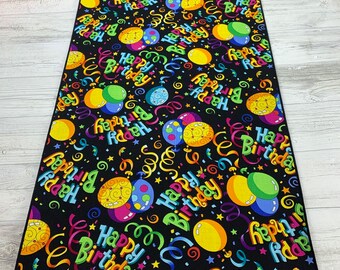 Puede incluir: Un camino de mesa negro con un patrón colorido de globos y confeti. Los globos tienen el texto "Happy Birthday" en ellos.