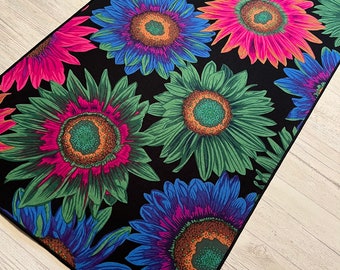 Puede incluir: Un camino de mesa negro con un patrón de girasol colorido. Los girasoles están en tonos de rosa, azul, verde y naranja.