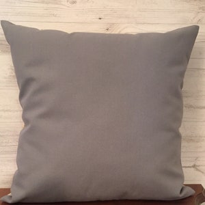Puede incluir: Una almohada de tiro gris lisa con forma cuadrada. La almohada est&aacute; hecha de una tela suave y lisa.