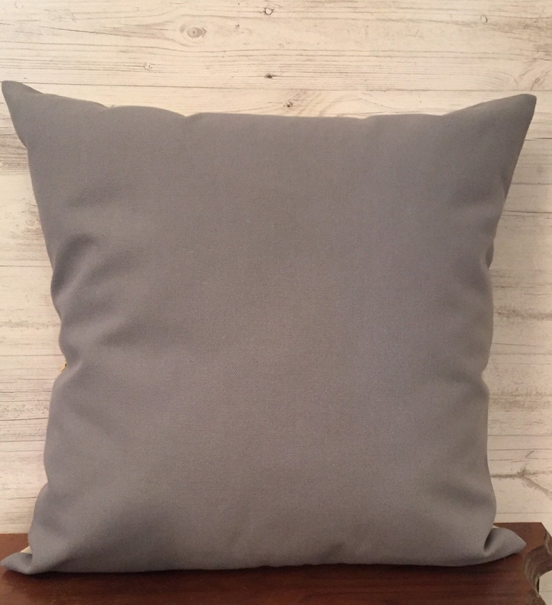 Puede incluir: Una almohada de tiro gris lisa con forma cuadrada. La almohada est&aacute; hecha de una tela suave y lisa.