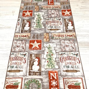 May include: A Christmas themed runner with a gray background and a variety of red, white, and green Christmas signs. The signs feature phrases like "Christmas Cookies for Sale", "Peace on Earth", and "Have Yourself a Merry Little Christmas".