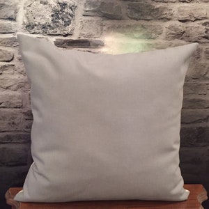 Puede incluir: Una almohada de tiro de color gris claro liso con un borde blanco. La almohada est&aacute; sobre una superficie de madera.