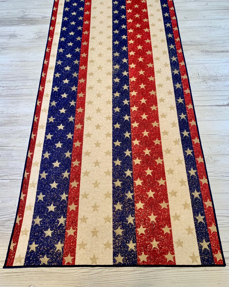 May include: A red, white, and blue striped runner with a glittery finish. The runner features a repeating pattern of stars.